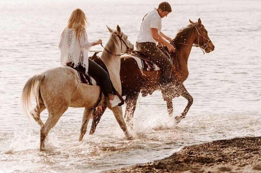 Deux personnes montent à cheval sur une plage, et l’eau éclabousse tout autour d’elles. 2