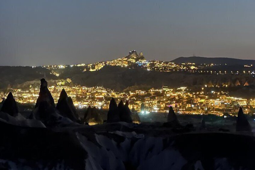 Una città illuminata di notte, con luci su una collina e coni innevati in primo piano. 4