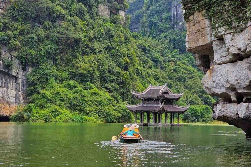 Un pavillon chinois traditionnel, construit sur pilotis au-dessus de l’eau, entouré d’une végétation luxuriante et de falaises rocheuses. 4