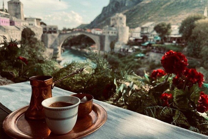 Een mooi uitzicht op een rivier met een brug, een kop koffie en rode bloemen op een tafel. 1