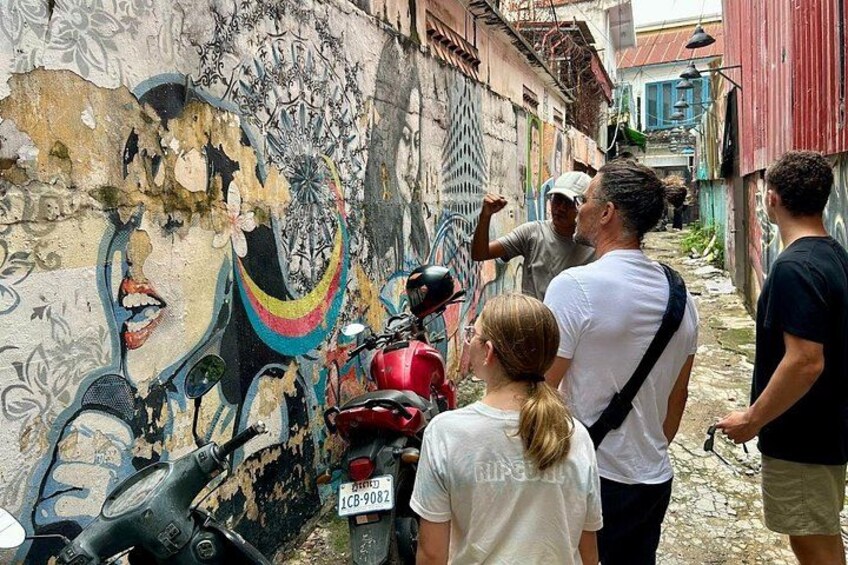 A mural on a wall, a red motorcycle, and people standing nearby. 4