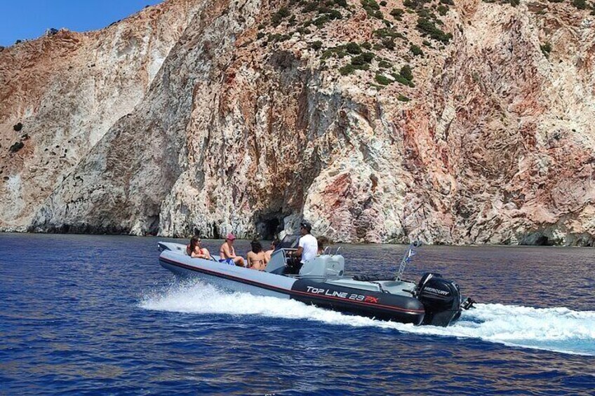 A speedboat with people on board, moving through a body of water with rocky cliffs in the background. 3