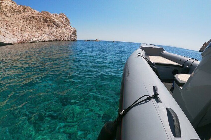 A clear blue sea with a rocky coastline and a white inflatable boat. 2