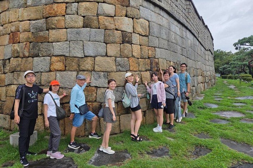 A group of people standing against a stone wall in a grassy area. 3