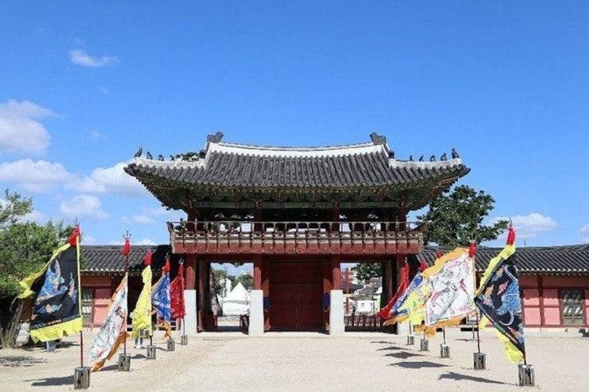 A traditional Korean gate with a tiled roof, surrounded by flags. 4