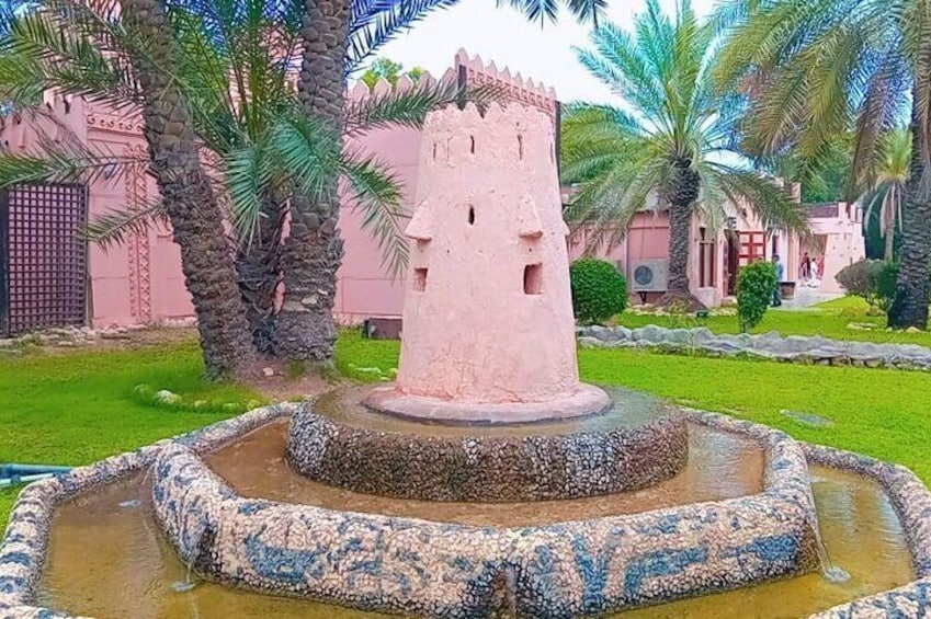 Une structure rose en forme de tour, située dans un jardin agrémenté de palmiers et d’une fontaine. 4