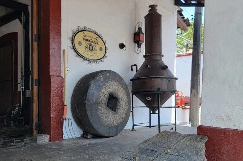 Un'ambientazione rustica all'aperto con un grande stufa in metallo, una grande ruota e una targa appesa al muro. 3
