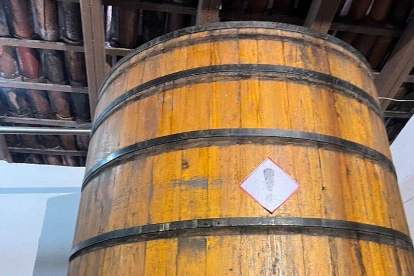 Un'ampia botte di legno con fasce metalliche e un cartello di avvertimento a forma di diamante. 5