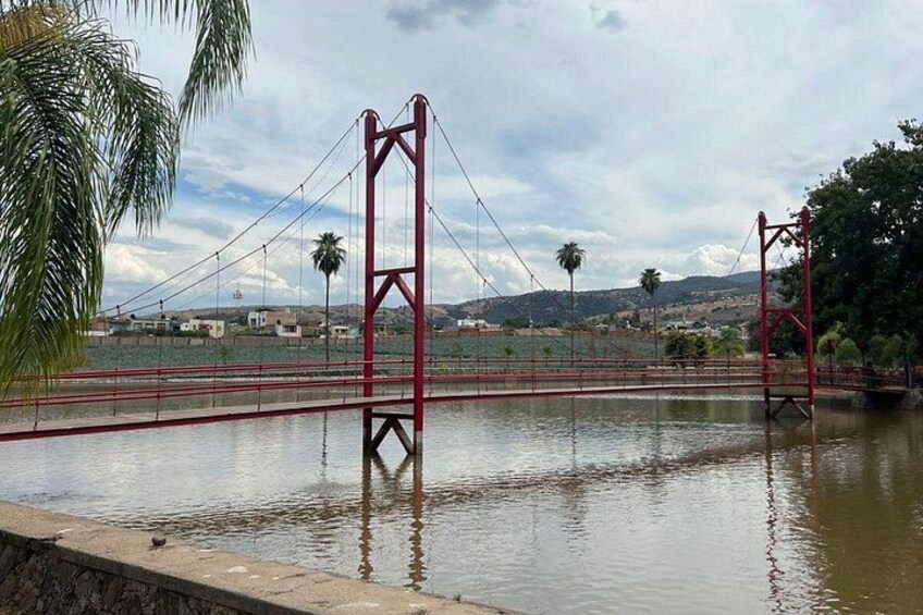 Un ponte sospeso rosso che sovrasta una distesa d'acqua, con palme e colline in lontananza. 2