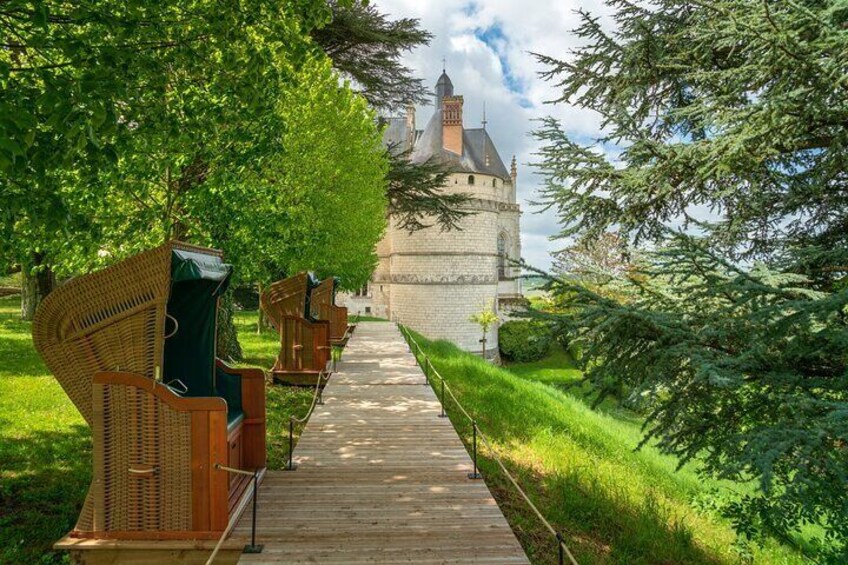 A wooden boardwalk leading to a castle with a turret, surrounded by lush greenery and trees. 2