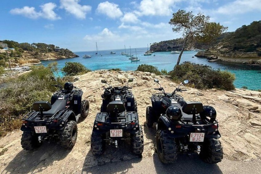 Tre fyrhjulingar parkerade på en stenig strand, med båtar i bakgrunden. 1