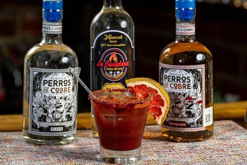 Drie tequilaflessen en een glas rode cocktail, versierd met garnering. 1