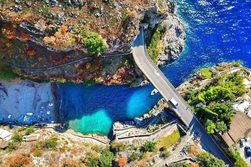 A coastal road winding through a rocky landscape with a clear blue sea. 1