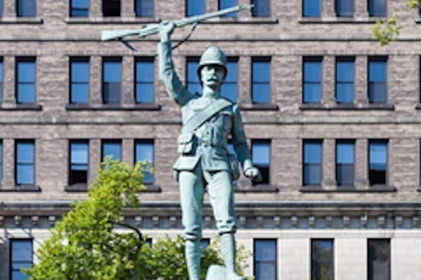 Une statue d’un soldat tenant un fusil devant un bâtiment doté de nombreuses fenêtres. 1
