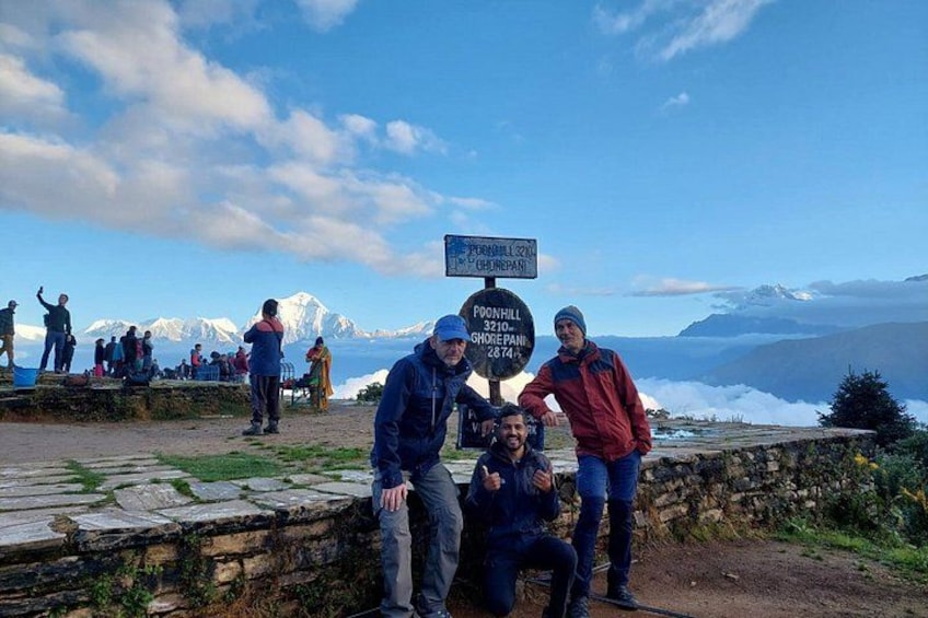 A group of people at a mountain viewpoint with a sign indicating Foon Hill and a distance marker. 2
