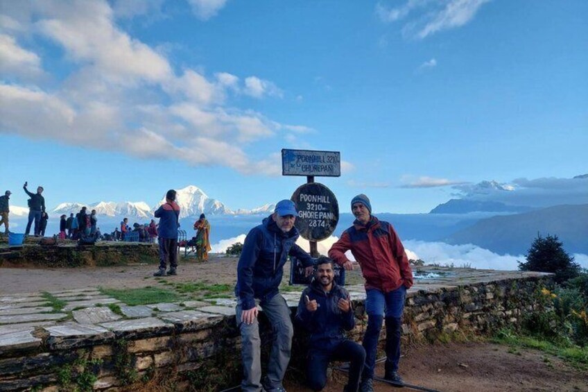 Un groupe de personnes se trouve sur un point de vue en montagne, près d’un panneau indiquant l’altitude de Poon Hill et la distance qui les sépare de la ville la plus proche. 2