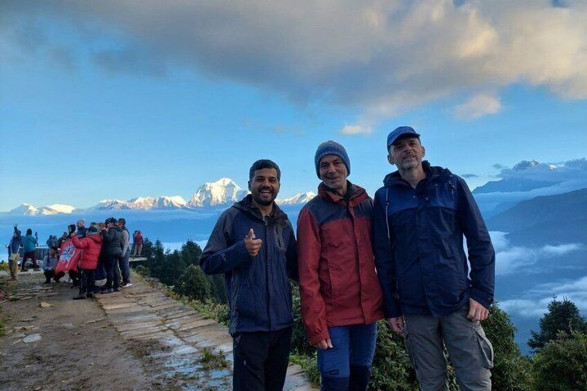Trois personnes se tiennent sur un sentier de montagne, avec une vue sur des montagnes enneigées et une vallée en contrebas. 4