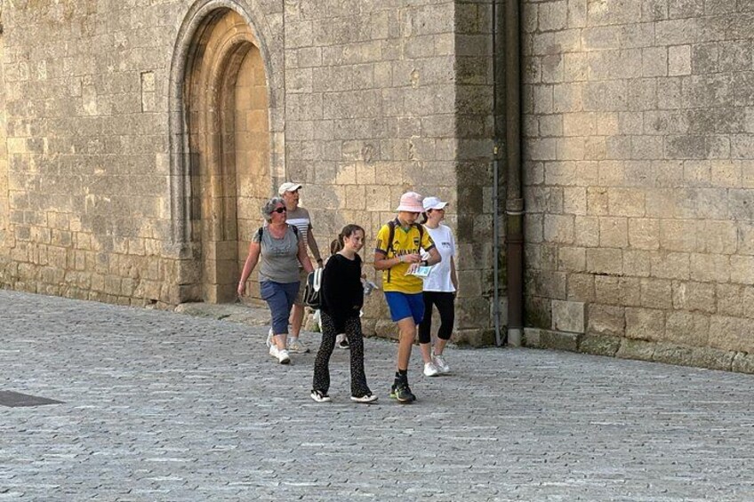 A group of people walking on a cobblestone street in front of a stone building with an arched doorway. 3