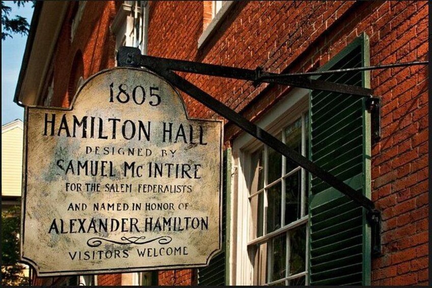 Un cartel histórico de Hamilton Hall, diseñado por Samuel McIntire, que data de 1805, ubicado en un edificio con contraventanas verdes. 1