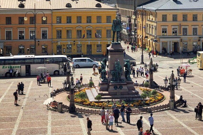 A public square with a central monument, surrounding buildings, and a bus. 2