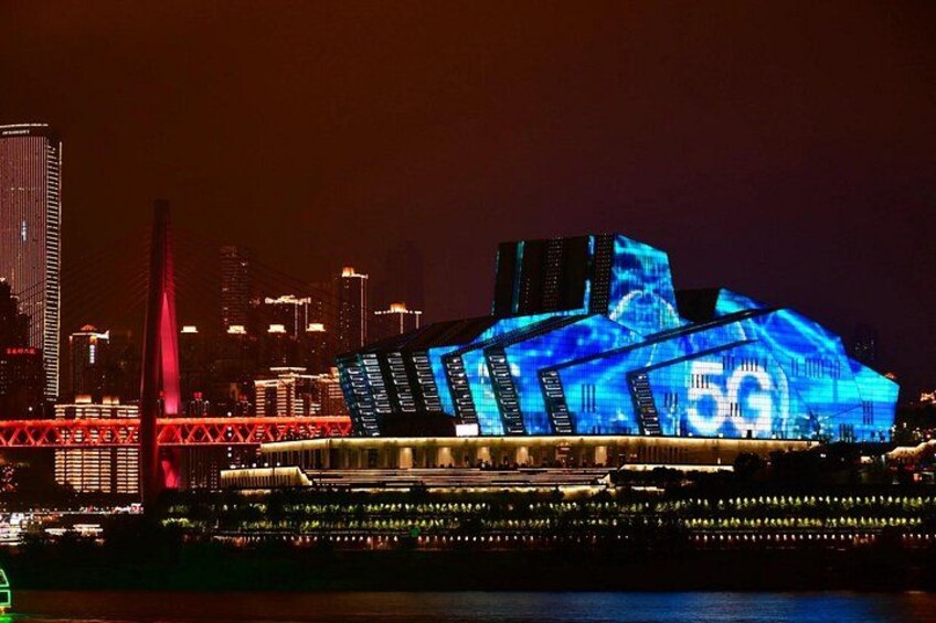 A brightly lit building with a 5G symbol, a red bridge, and city skyline in the background. 5