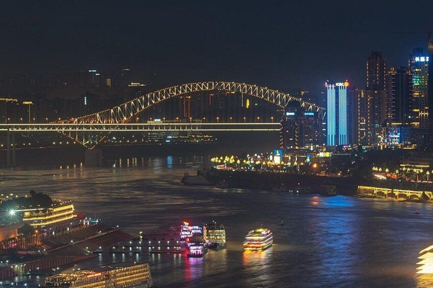 A nighttime cityscape with a prominent bridge, illuminated buildings, and a river with boats. 4