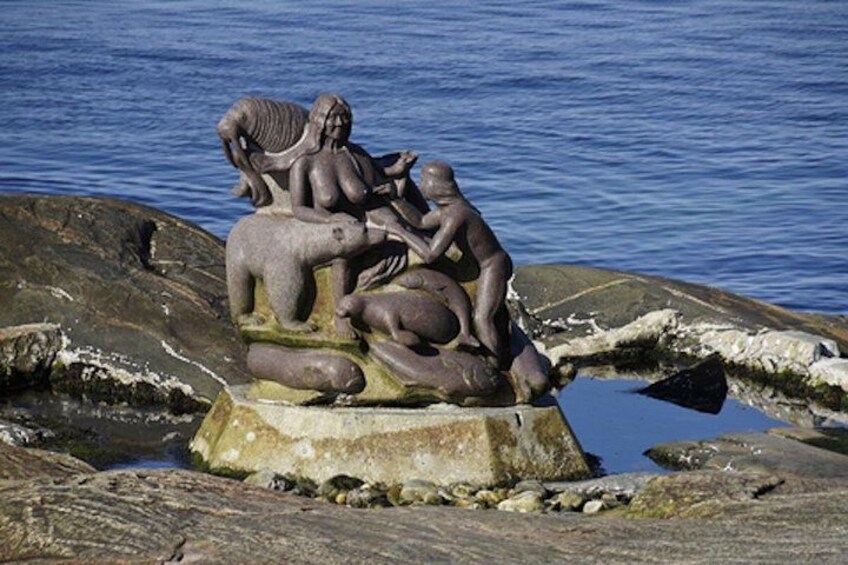 A sculpture of figures on a rock by the water. 2
