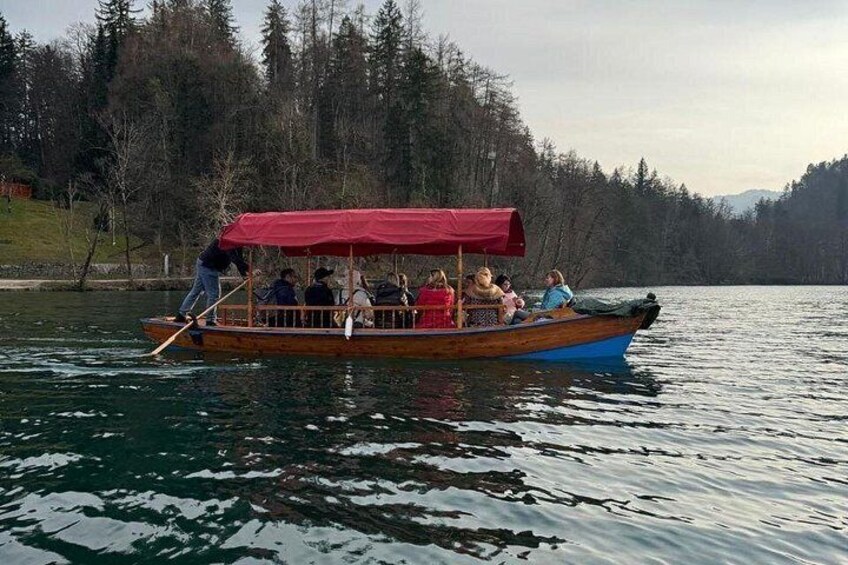 Een houten boot met een rood zonnescherm, mensen aan boord en een bebost oever in de verte. 4