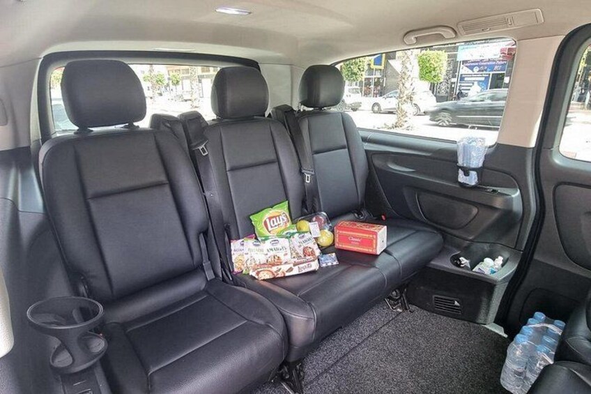 A car interior with black leather seats, a rear seat console with snacks, and a water bottle. 5