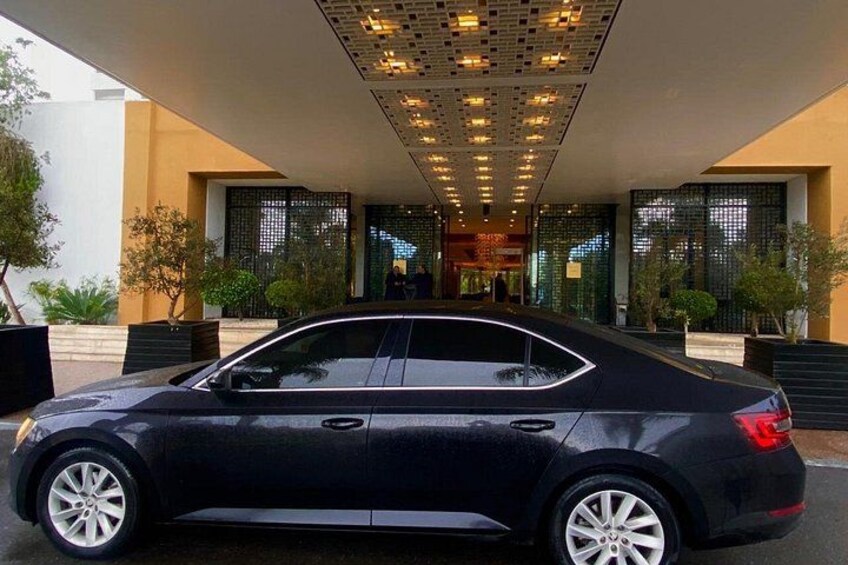 A black car parked in front of a modern building with a glass facade and a patterned ceiling. 4