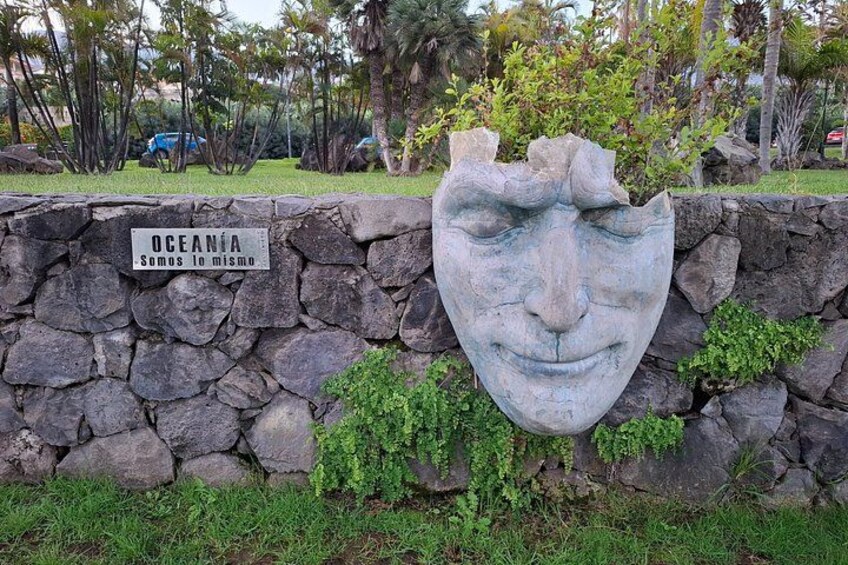 Eine steinerne Mauer mit einem eingemeißelten Gesicht und einem Schild, auf dem 'OCEANIA Somos lo mismo' steht. 2