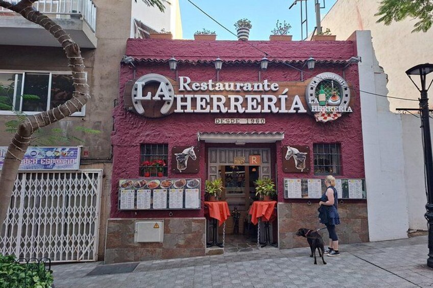 Ein Restaurant namens Restaurante Herrería mit roter Fassade und einem angeleinten Hund vor der Tür. 3