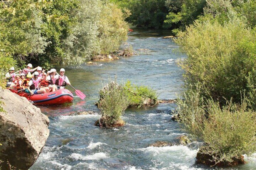 A group of people in a red raft navigating a river surrounded by greenery. 5