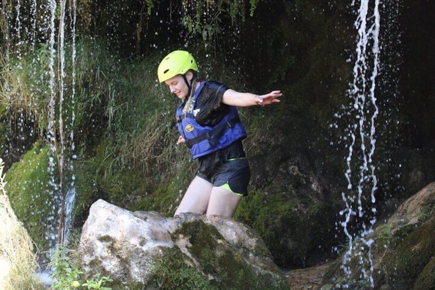 A person in a helmet and life jacket standing on a rock by a waterfall. 3
