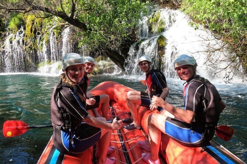Eine Gruppe von Menschen in einem Floß auf einem Fluss, im Hintergrund ein Wasserfall. 3