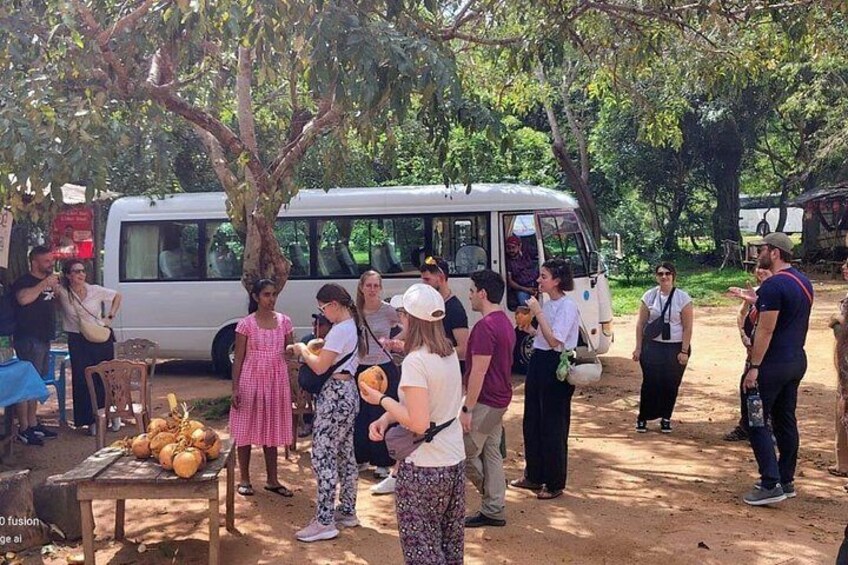 Eine Gruppe von Menschen versammelt sich um einen Imbisswagen, mit einem Bus und Bäumen im Hintergrund. 1