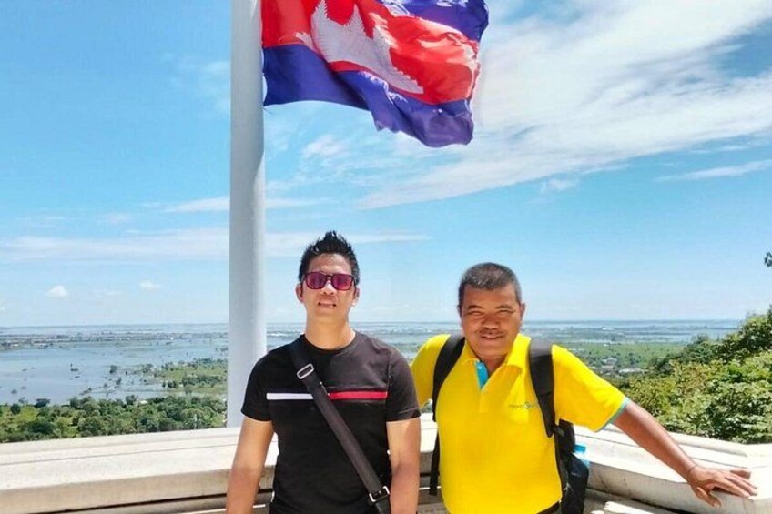 Two people standing near a flagpole with a scenic view of a body of water and greenery in the background. 3