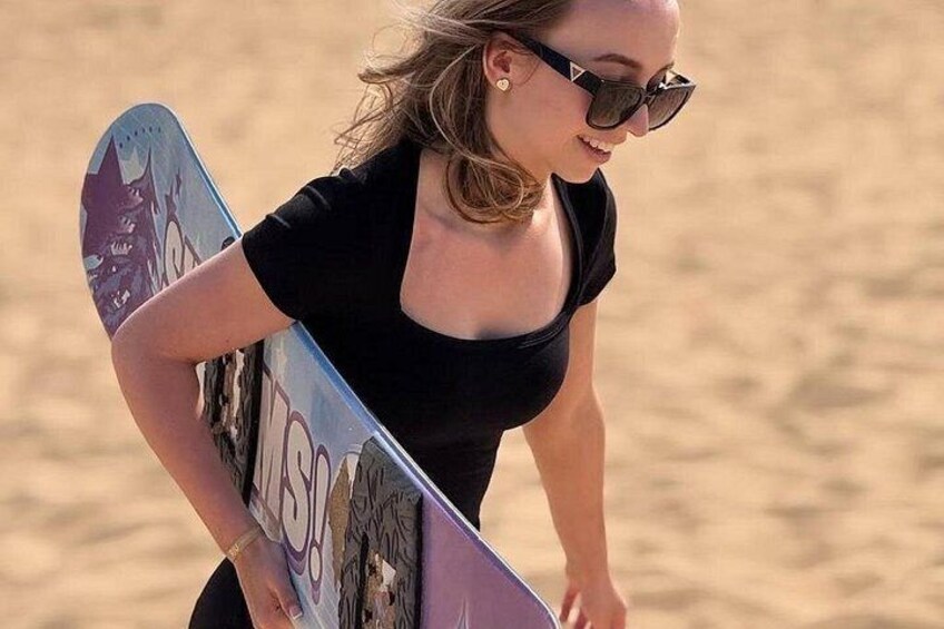 Una persona che tiene uno snowboard con una grafica, in piedi su una superficie sabbiosa. 1