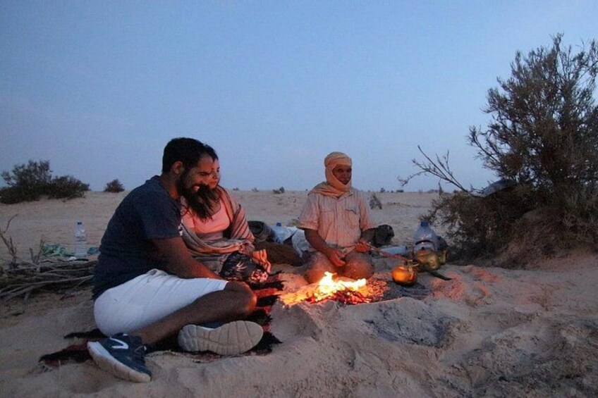 Zwei Personen sitzen am Strand in der Nähe eines Lagerfeuers. 4