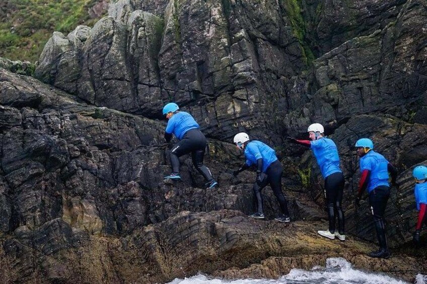 A group of people in blue shirts and helmets climbing a rocky cliff. 3