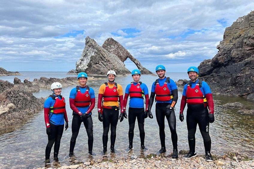 A group of people in blue and red life jackets standing by a rocky shoreline. 4