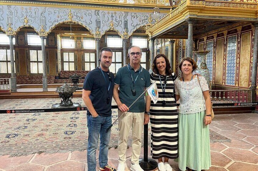 A group of people standing in a grand hall with ornate decorations and a fountain in the background. 1