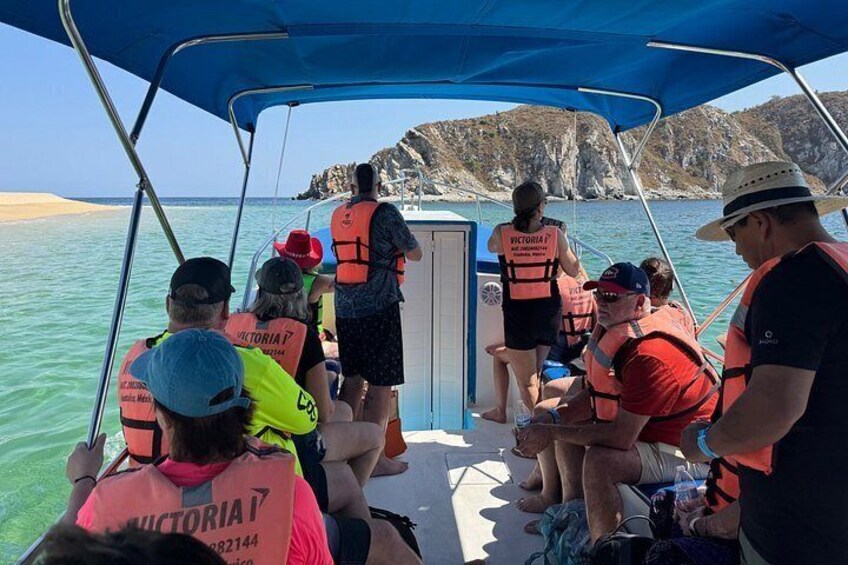 A group of people on a boat wearing life jackets, with a rocky coastline in the background. 1