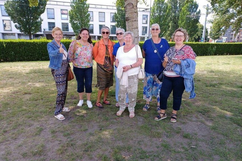 Un grupo de personas de pie sobre césped en un entorno al aire libre, con árboles y edificios al fondo. 2