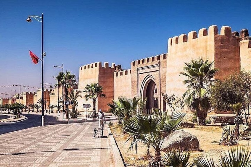 A fortified building with a large archway, palm trees, and a clear blue sky. 1