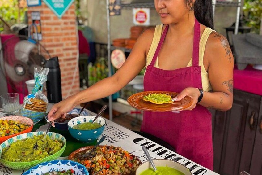 A person serving food at an outdoor event with various dishes and a sign that reads 'COLABOCA'. 4