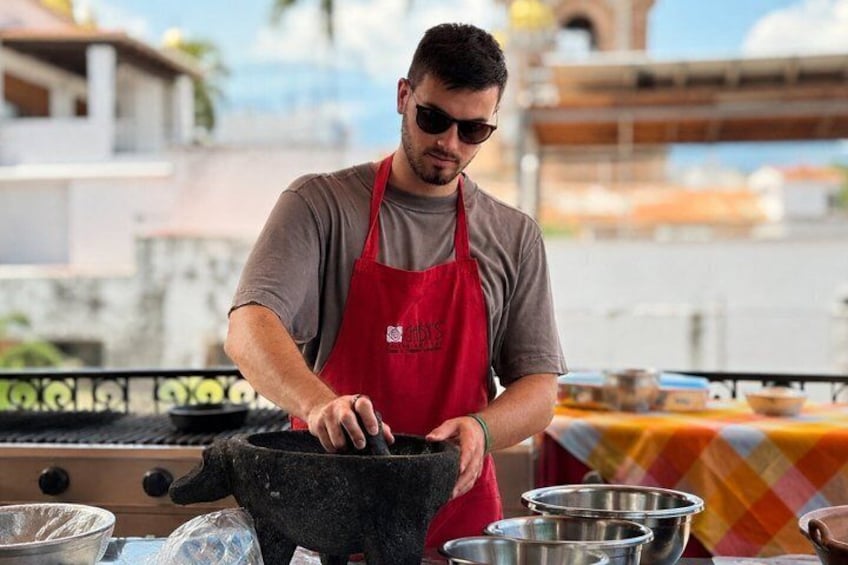 Una persona cucina all'aperto, indossa un grembiule rosso, con utensili da cucina e una griglia in vista. 3
