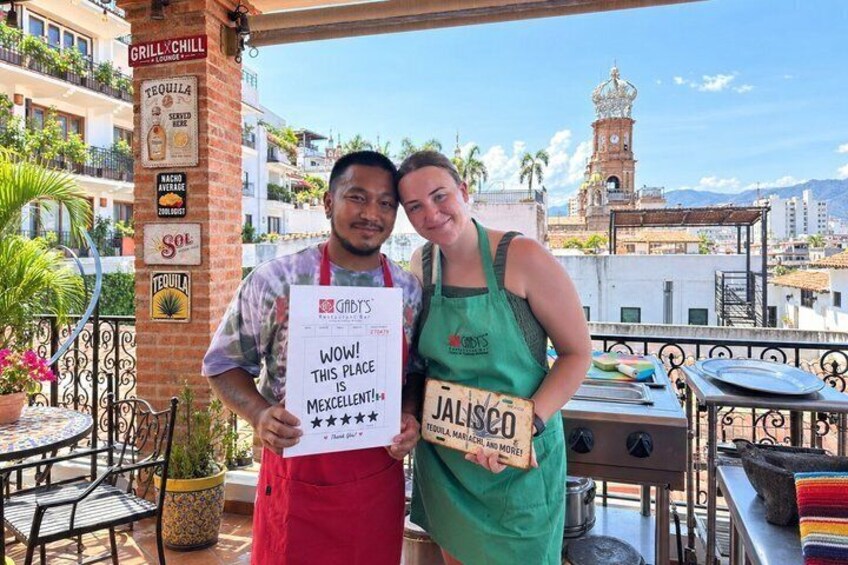 Deux personnes sur une terrasse d’un immeuble, avec une pancarte sur laquelle on peut lire : « WAOUH ! CET ENDROIT EST GÉNIAL !! ». 2