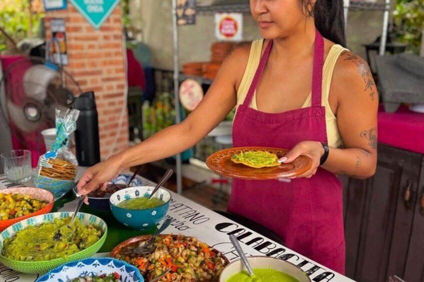 A person serving food at an outdoor event with various dishes and a sign that reads 'COLABOCA'. 4