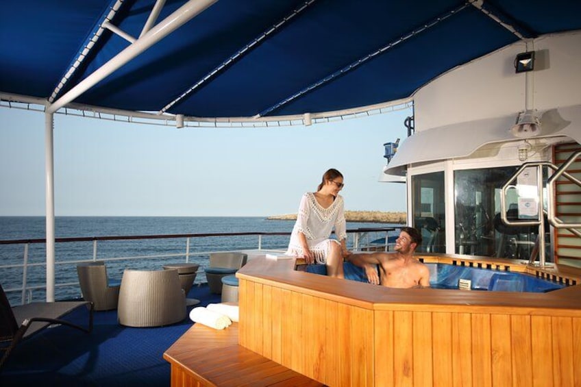 A wooden hot tub on a boat deck with a person sitting and another person standing. 4